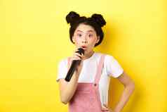 可爱的亚洲青少年女孩明亮的化妆唱歌麦克风卡拉ok站黄色的背景