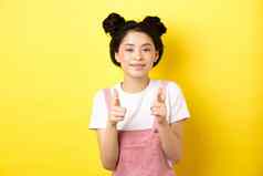 快乐的青少年亚洲女孩指出手指相机微笑鼓励邀请使赞美赞美不错的工作站黄色的背景