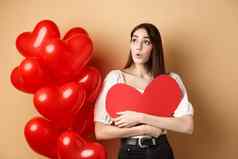 情人节一天爱概念感兴趣温柔的女孩拥抱大红色的心断路站气球标志哇米色背景