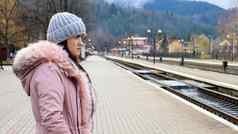 女人灰色的针织他粉红色的夹克皮毛等待火车站铁路运输秋天冬天旅行概念