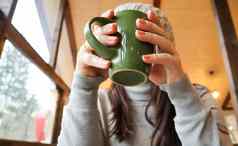 关闭女手喝杯子女孩灰色的毛衣持有杯咖啡可可咖啡馆表格窗口热喝舒适的照片模糊的背景