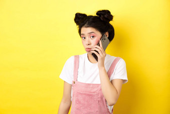 可爱的青少年女孩会说话的智能手机使愚蠢的撅嘴脸胆小相机站魅力化妆黄色的背景