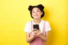可爱的时尚的亚洲女孩移动电话穿魅力粉红色的化妆夏天衣服站黄色的背景