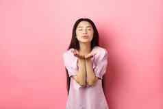 可爱的浪漫的亚洲女孩吹空气吻相机关闭眼睛微笑温柔站衣服粉红色的背景
