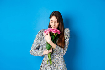 情人节一天概念充满激情的浪漫的年轻的女人拥抱花束礼物玫瑰闻花情人站蓝色的背景