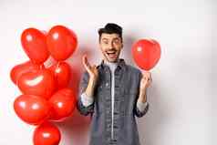 情人节一天概念快乐的年轻的男人。庆祝爱假期站红色的心气球惊讶尖叫快乐白色背景