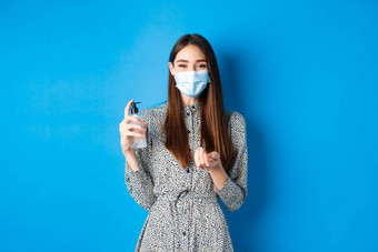 科维德社会距离医疗保健概念美丽的女孩医疗面具手消毒剂持有防腐剂瓶站蓝色的背景