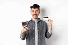 在线购物概念兴奋男人。使购买互联网容易购买塑料信贷卡智能手机微笑快乐相机白色背景