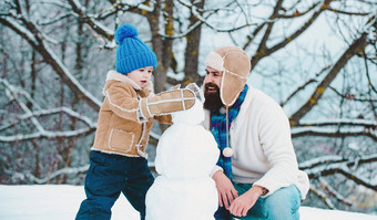 冬天父亲儿子玩outdoo使雪人手工制作的有趣的雪男人。圣诞节家庭假期爸爸