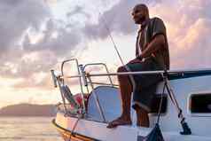 年轻的非洲美国男人。站钓鱼杆帆船钓鱼开放海日落