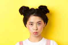 关闭肖像喜怒无常的亚洲女孩撅嘴心烦意乱相机站wiht魅力化妆发髻黄色的背景