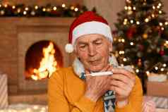 不健康的高级男人。圣诞老人他坐着壁炉包装围巾持有温度计手发热摆姿势节日房间圣诞节装饰壁炉
