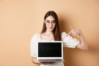 自信年轻的女人眼镜指出移动PC屏幕显示电脑显示站米色背景