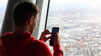 年轻的男人。使照片城市景观智能手机旅游概念男人。照片城市观察甲板玻璃高度