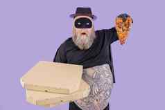震惊了丰满男人。英雄服装持有盒子片披萨紫色的背景