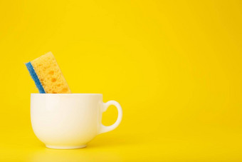 有创意的最小的洗碗概念黄色的清洁海绵白色陶瓷杯黄色的背景复制空间