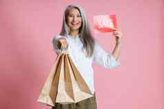 亚洲女人持有购物袋红色的卡wirh词出售粉红色的背景