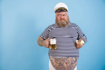 有趣的肥胖水手持有吸烟管啤酒扮鬼脸光蓝色的背景