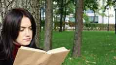 肖像美丽的年轻的女人坐着树阅读最喜欢的书城市公园绿色草愉快的阳光明媚的一天假期教育研究概念