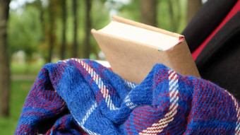 书蓝色的网纹羊毛毯子格子手女人穿毛衣黑色的外套公园温暖的阳光明媚的天气软舒适的照片特写镜头