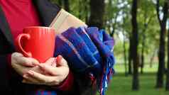 红色的杯咖啡书蓝色的网纹羊毛毯子格子手女人穿毛衣黑色的外套公园温暖的阳光明媚的天气软舒适的摄影