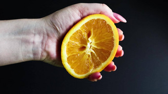 女手挤压一半新鲜的多汁的橙色柑橘类橙色汁滴橙色纸浆黑色的背景概念健康的饮食饮食准备让人耳目一新喝