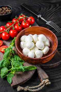 意大利迷你马苏里拉奶酪奶酪球罗勒番茄樱桃准备好了烹饪它们沙拉黑色的木背景前视图