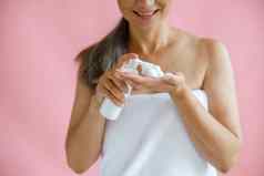 微笑中间岁的夫人毛巾挤压身体护理产品手粉红色的背景