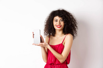 优雅的女人红色的衣服化妆显示空白智能手机屏幕微笑站白色背景