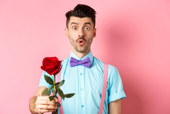 情人节一天浪漫概念可爱的男人。蝴蝶结给红色的玫瑰同情站浪漫的粉红色的背景