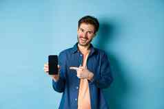 微笑高加索人男人。显示空智能手机屏幕指出移动电话满意站蓝色的背景
