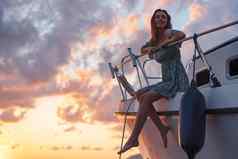 年轻的有吸引力的女人坐着甲板游艇享受日落