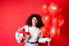 兴奋美丽的女人庆祝情人节一天假期持有礼物盒子浪漫的心气球惊讶相机站红色的背景