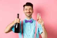 假期庆祝活动概念快乐男人。微笑享受喝聚会，派对持有瓶香槟玻璃站粉红色的背景