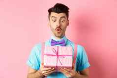 假期庆祝活动概念英俊的的家伙蝴蝶结接收生日礼物现在包装盒子好奇的惊讶脸粉红色的背景