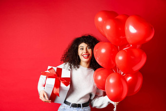 假期庆祝活动快乐生日女孩持有礼物摆姿势聚会，派对氦气球微笑兴奋相机红色的背景