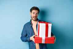 英俊的有胡子的的家伙持有情人节一天礼物情人站礼物盒子相机蓝色的背景