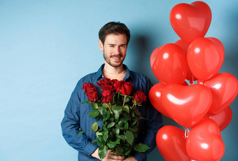 浪漫的的男朋友眨眼微笑持有花束花情人节一天站<strong>心气球</strong>情人蓝色的背景