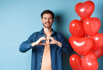 快乐情人节一天的男朋友爱显示心手势情人微笑站红色的气球蓝色的背景