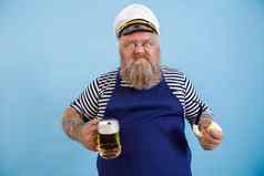 有趣的肥胖水手围裙持有管美味的啤酒光蓝色的背景