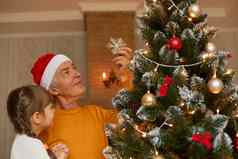 成熟的男人。圣诞老人老人他橙色衬衫装修冷杉树持有（外）孙女手孩子爷爷摆姿势生活房间