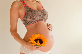 怀孕了女孩拥抱肚子持有黄色的向日葵手孕妇肚子皮肤治疗