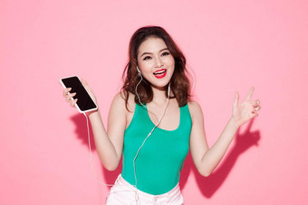 快乐快乐的亚洲女人穿无线耳机听音乐智能手机工作室拍摄孤立的粉红色的背景