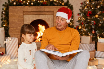 祖父穿橙色毛衣圣诞<strong>老人老人</strong>他阅读书可爱的（外）孙女坐着节日<strong>生活</strong>房间壁炉圣诞节树