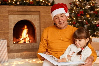 积极的高级男人。穿橙色毛衣圣诞<strong>老人老人</strong>他阅读仙女演讲迷人的（外）孙女摆姿势<strong>生活</strong>房间壁炉圣诞节树
