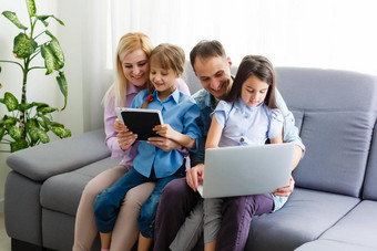 快乐家庭父母可爱的孩子们孩子们享受平板电脑看漫画使互联网视频调用购物在线电脑屏幕坐首页