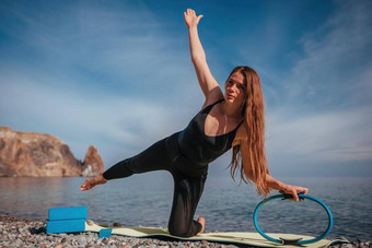 年轻的女人长头发健身教练黑色的运动服装<strong>紧身</strong>裤上衣伸展运动瑜伽席魔法普拉提环海阳光明媚的一天女健身瑜伽例程概念