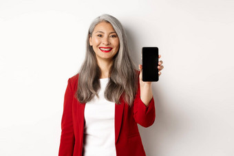 上了年纪的女商人红色的夹克显示空白智能<strong>手机</strong>屏幕微笑<strong>演示</strong>移动应用程序白色背景
