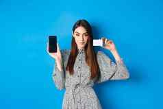 在线购物自信美女人显示塑料信贷卡空智能手机屏幕显示停止站蓝色的背景