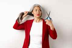 优柔寡断亚洲女人持有剪刀怀疑思考减少头发改变发型站白色背景